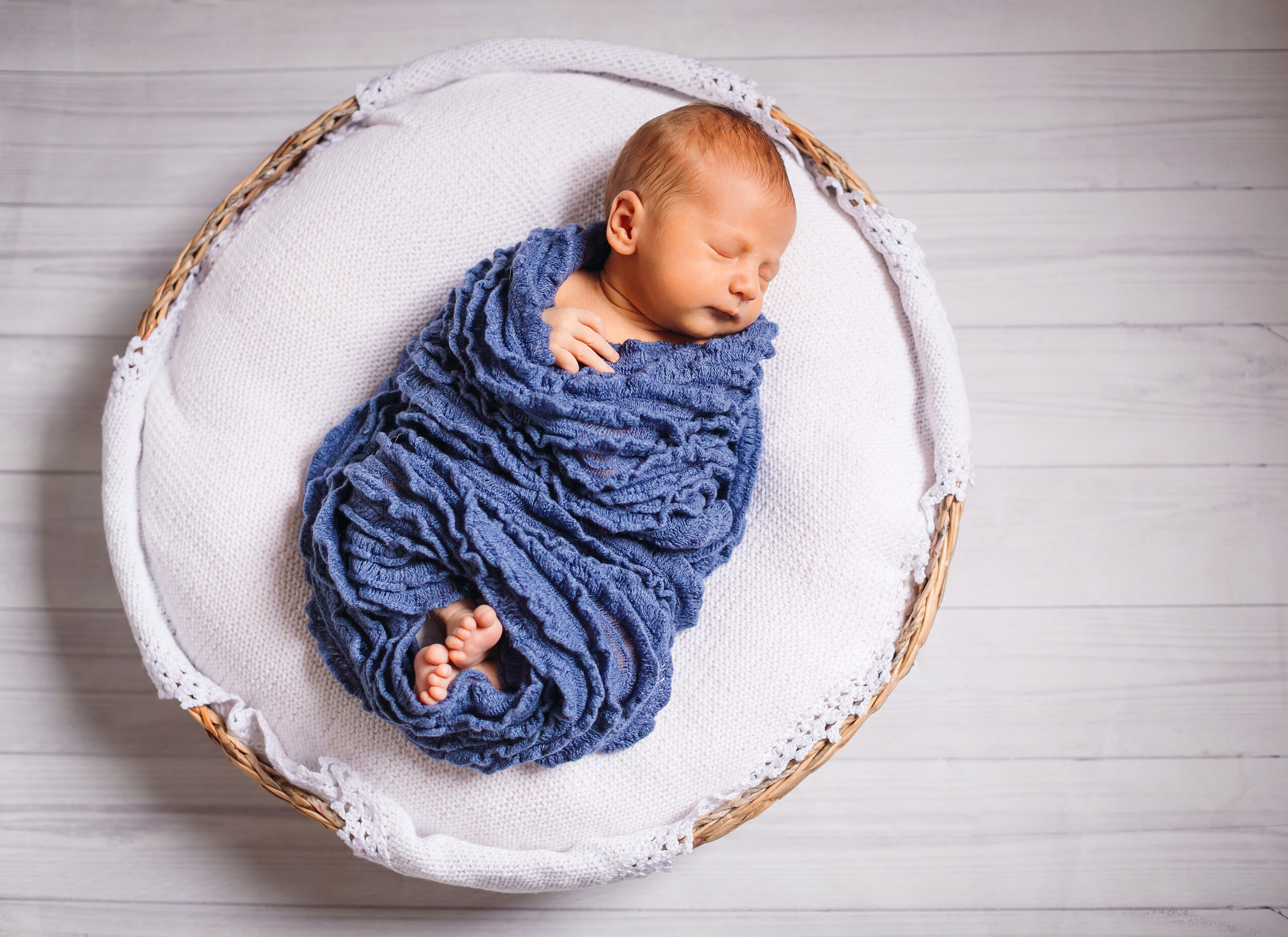 Newborn baby enveloped in blue scarf sleeps on white pillow